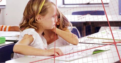 Young student leaning toward classmate collaborating over math worksheets in classroom