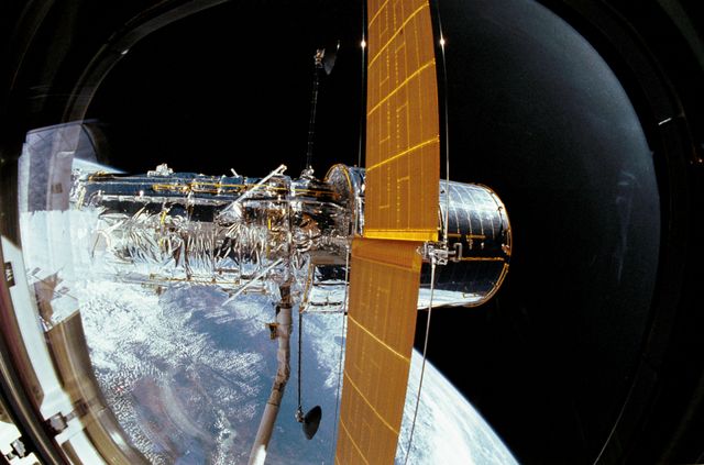 Hubble Space Telescope docked in space shuttle Discovery's bay, described during 1990's mission STS-31. Hubble's solar array partially deployed above Earth. NASA space mission illustrating historic context offers visuals for space exploration projects, educational materials, films, documentaries, space science presentations.