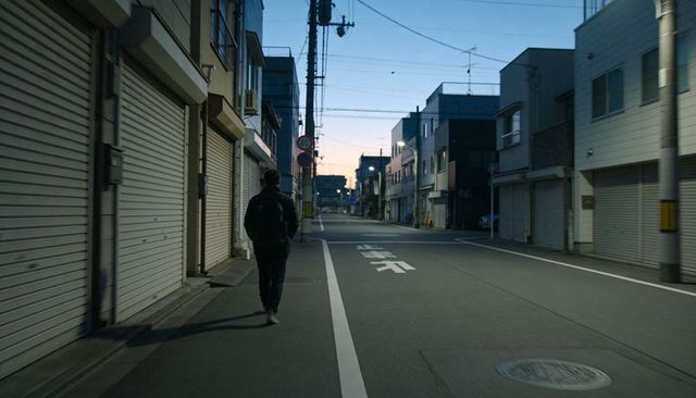 Solo man walking down closed-shop urban street at twilight with backpack and power lines