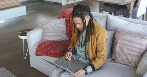 African American man working on laptop on sofa, remote work concentration in modern livingroom