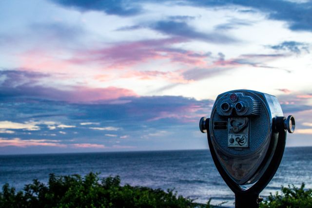 Coin-operated binoculars looking out over ocean during beautiful sunset, with vibrant sky and clouds in background. Perfect for use in tourism promotions, travel blogs, nature websites, and landscape photography prints.