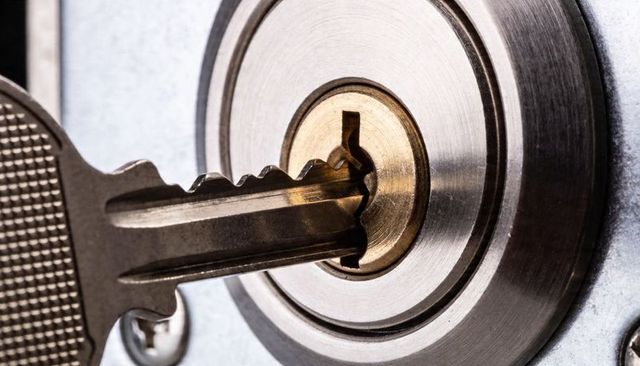Inserting key into deadbolt lock, brass keyway and stainless cylinder macro detail