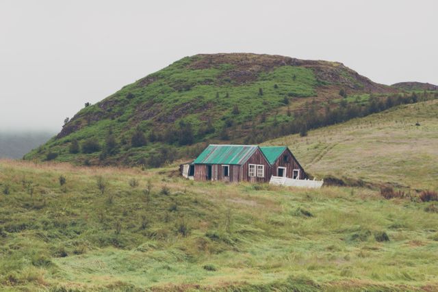 Rustic cabin nestled in foggy green hills creates tranquil countryside atmosphere. Suitable for nature travel blogs, rural living promotions, serene landscape posters, and escape from city adverts.