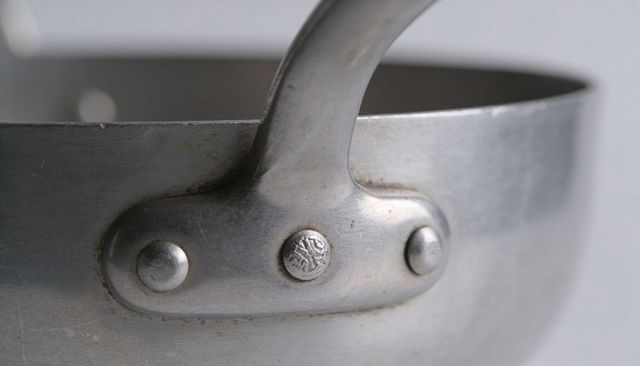 Close-up showing stainless saucepan riveted handle with brushed metal texture and wear