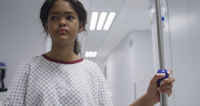 Biracial girl walking with drip bag in hospital room. medicine, health and healthcare services.