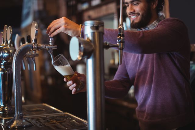 Bartender pouring draft beer into a glass at a bar counter. Ideal for use in articles or advertisements related to nightlife, pubs, bars, hospitality industry, and beverage services. Can also be used to depict friendly and casual service environments.