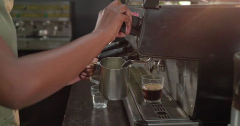 Barista preparing espresso and steaming milk with metal pitcher at commercial espresso machine
