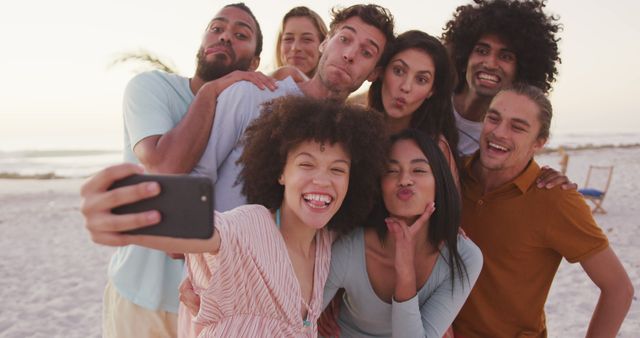 Group of friends enjoying their time at the beach during sunset, capturing memories by taking a selfie. Perfect for themes related to friendship, vacations, social media connection, and relaxed lifestyles. Suitable for travel blogs, advertisements for beach resorts, and social media campaigns emphasizing fun and togetherness.