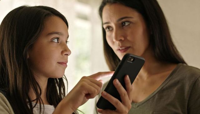 Mother and daughter sharing smartphone moment at home, daughter pointing and teaching
