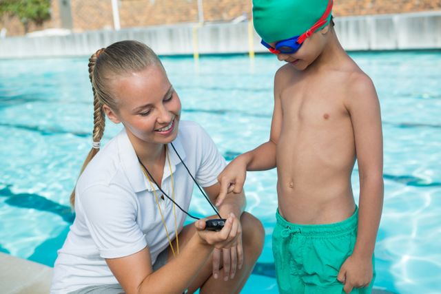 Female trainer showing stopwatch to boy at poolside