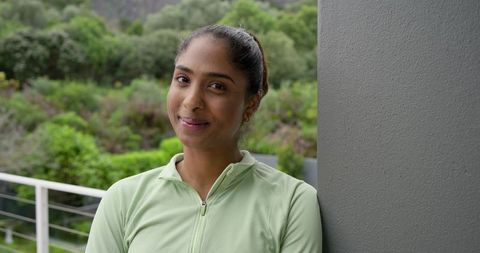 Indian woman leaning on balcony column smiling in light green zip-up top, serene portrait