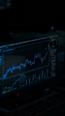Vertical video displaying live market analytics on trading monitors with backlit keyboard