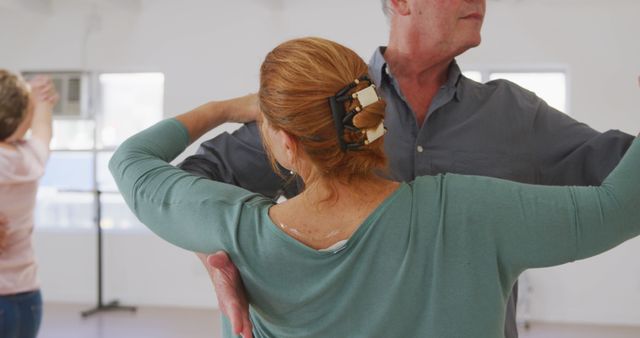 Senior couple is practicing ballroom dancing in a bright, spacious dance studio. Elderly man and woman are showcasing dance poses and movements, highlighting intimate connection and teamwork. Ideal for fitness, health, active lifestyle, and dance instruction related materials.