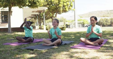 Preteen girls practicing outdoor yoga and mindfulness on mats in school park