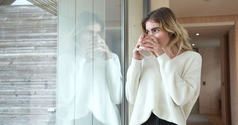 Woman in Knit Sweater Enjoying Hot Beverage by Cabin's Glass Door