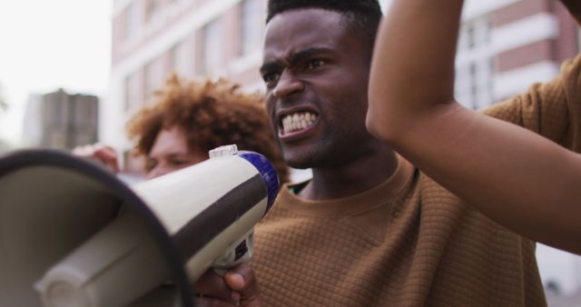 African american man shouting using megaphone with other people raising fists during protest. equal rights and justice protestors on demonstration march.