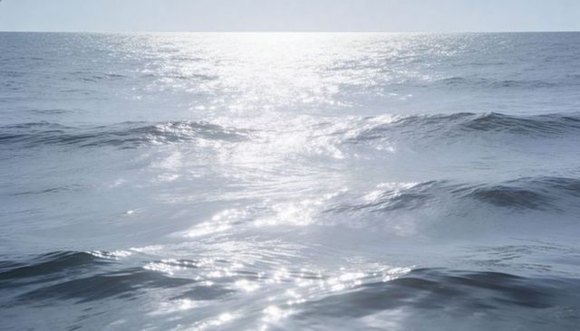 Shimmering ocean surface reflecting sunlight toward horizon with calm blue wave crests
