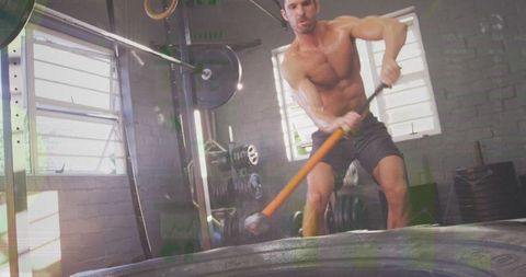 Shirtless athlete swinging sledgehammer on tire workout