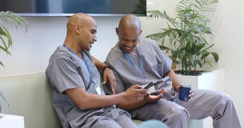African american male medical staff relaxing in clinic breakroom sharing smartphone and coffee