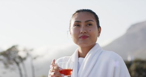 Asian woman enjoying morning terrace drink in white robe with mountain mist backdrop