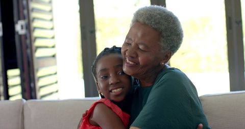 Senior woman hugging young girl on sofa, intergenerational family embrace at home