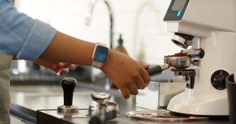 Female barista preparing portafilter under grinder, tamping coffee at countertop