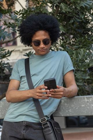African american man checking smartphone while leaning on concrete railing in city