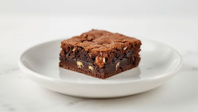 Fudgy chocolate brownie with chopped nuts on white plate decadent marble close-up