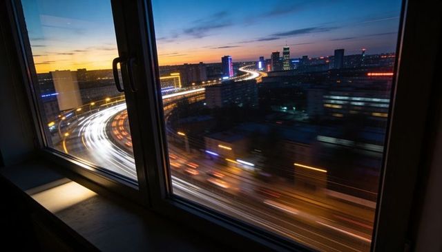 Curved elevated expressway light trails framed through window handle at twilight cityscape