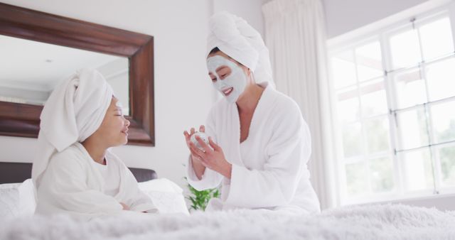 Image of happy asian mother and daughter in robes moisturizing faces and having fun. Family, motherhood, relations and spending quality time together concept digitally generated image.