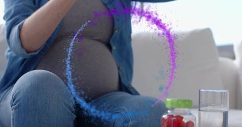 Pregnant woman in denim sitting on sofa using prenatal gummies with glowing belly arc