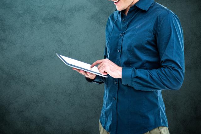 Man in blue shirt interacting with a tablet against grey background. Perfect for themes related to technology, digital communication, mobile applications, casual work settings, and modern office environments.