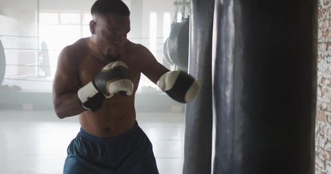 Shirtless boxer training in industrial gym throwing jab at heavy bag focused athlete