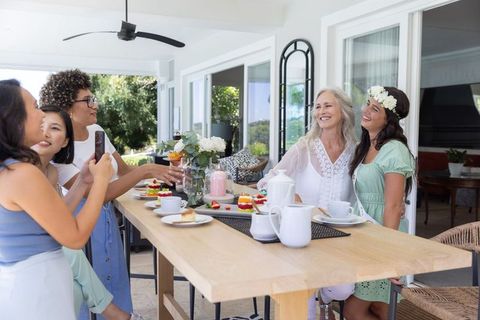 Multigenerational women celebrating bridal shower on sunny veranda with tea and cakes