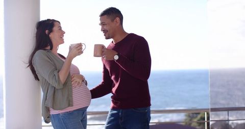 Couple enjoying coffee on oceanfront balcony during pregnant partner's getaway