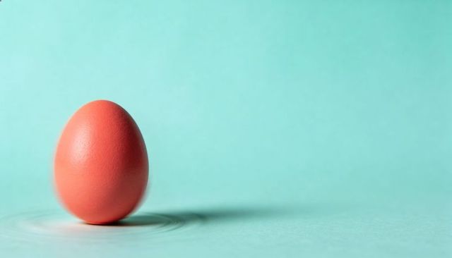 Minimal orange egg standing on mint backdrop with soft ripple shadow and pastel composition