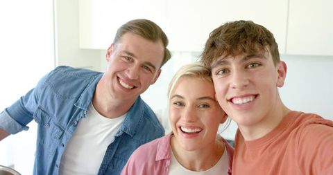 Smiling parents and teenage son in bright kitchen cooking together sharing joyful family moment