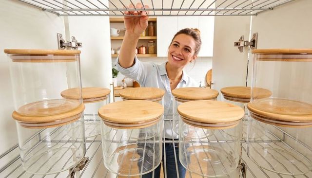 Smiling woman organizing pantry glass jars with bamboo lids in modern bright kitchen