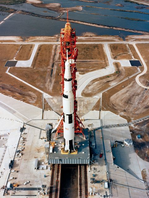 Aerial, high-angle view showing the Apollo 10 space vehicle on its launch pad at Kennedy Space Center in Florida. The scene captures the enormous scale of the Saturn V rocket and the launch facility's preparation for the mission. Ideal for use in articles about space exploration, NASA missions, or historical technological achievements.