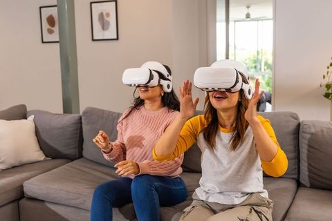 Diverse women enjoying immersive virtual reality experience on sofa using white vr headsets