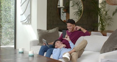 Friends Relaxing on Sofa with Gadgets in Modern Living Room