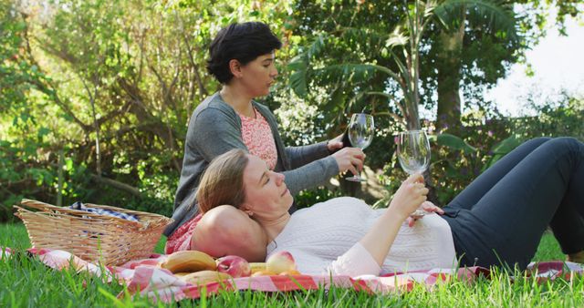 Caucasian lesbian couple drinking wine together in the garden during picnic. lgbt relationship and lifestyle concept
