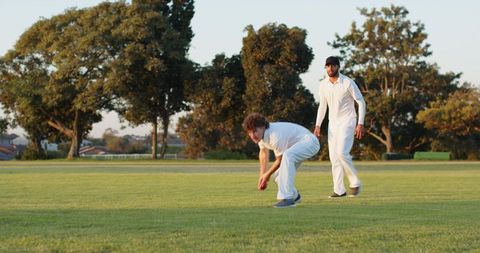 Two Cricketers Fielding on Outfield at Golden Hour Catching Red Ball in Suburban Park
