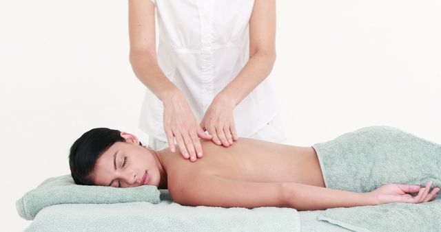 A Caucasian female massage therapist is providing a relaxing back massage to an Asian female client lying on a massage table, with copy space. The serene environment suggests a focus on wellness and self-care.