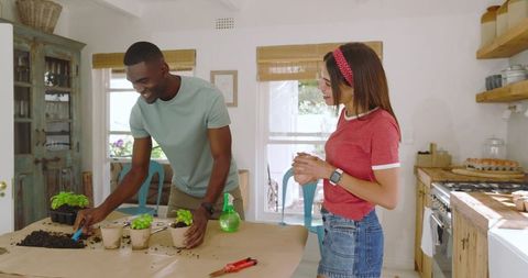 Diverse Couple Planting Seedlings Together in Home Kitchen for Sustainable Living