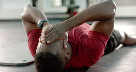 African american man lying on gym mat covering face after workout wearing fitness tracker