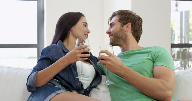 A young Caucasian couple enjoys a moment of closeness while holding glasses of wine, with copy space. Their cheerful interaction suggests a casual and intimate setting, reflecting a romantic relationship.