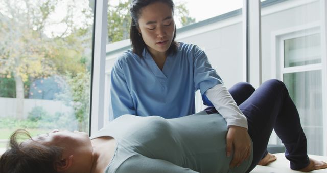 Asian female physiotherapist treating female patient lying on examination bed at surgery. physiotherapy, health and healthcare services.
