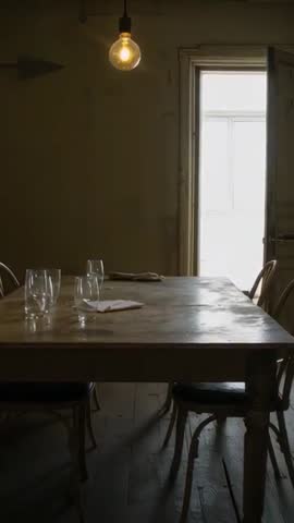 Vertical video flickering bulb casting warm glow over rustic wooden table, shifting glass glares