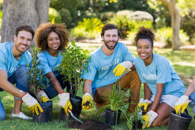Group of diverse young adults volunteering by planting trees in a park. They are smiling and wearing gloves, showing teamwork and community spirit. Ideal for use in articles or campaigns promoting environmental conservation, community service, teamwork, and social causes.